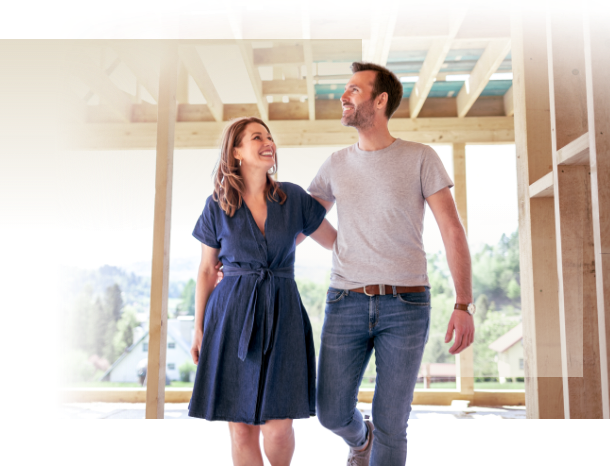 Bauen oder Kaufen – Lachendes Paar im Rohbau ihres neuen Hauses