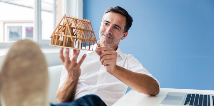 Bausparvertrag – Mann mit Model von Haus in der Hand