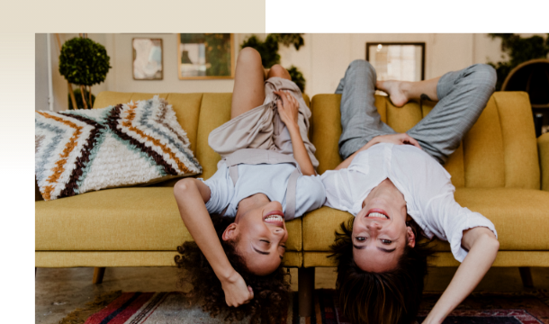 Zwei junge Frauen liegen falsch herum auf Sofa und lachen