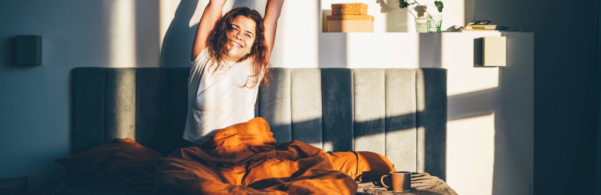 Glückliche Frau sitzt mit Kaffee im Bett