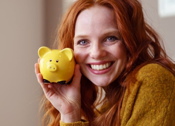 Anschlussfinanzierung – Lachende Frau mit Sparschwein in der Hand