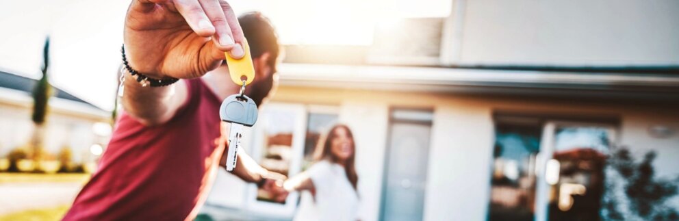 Finanzierung – Paar läuft mit Schlüssel in Hand zu neuem Haus